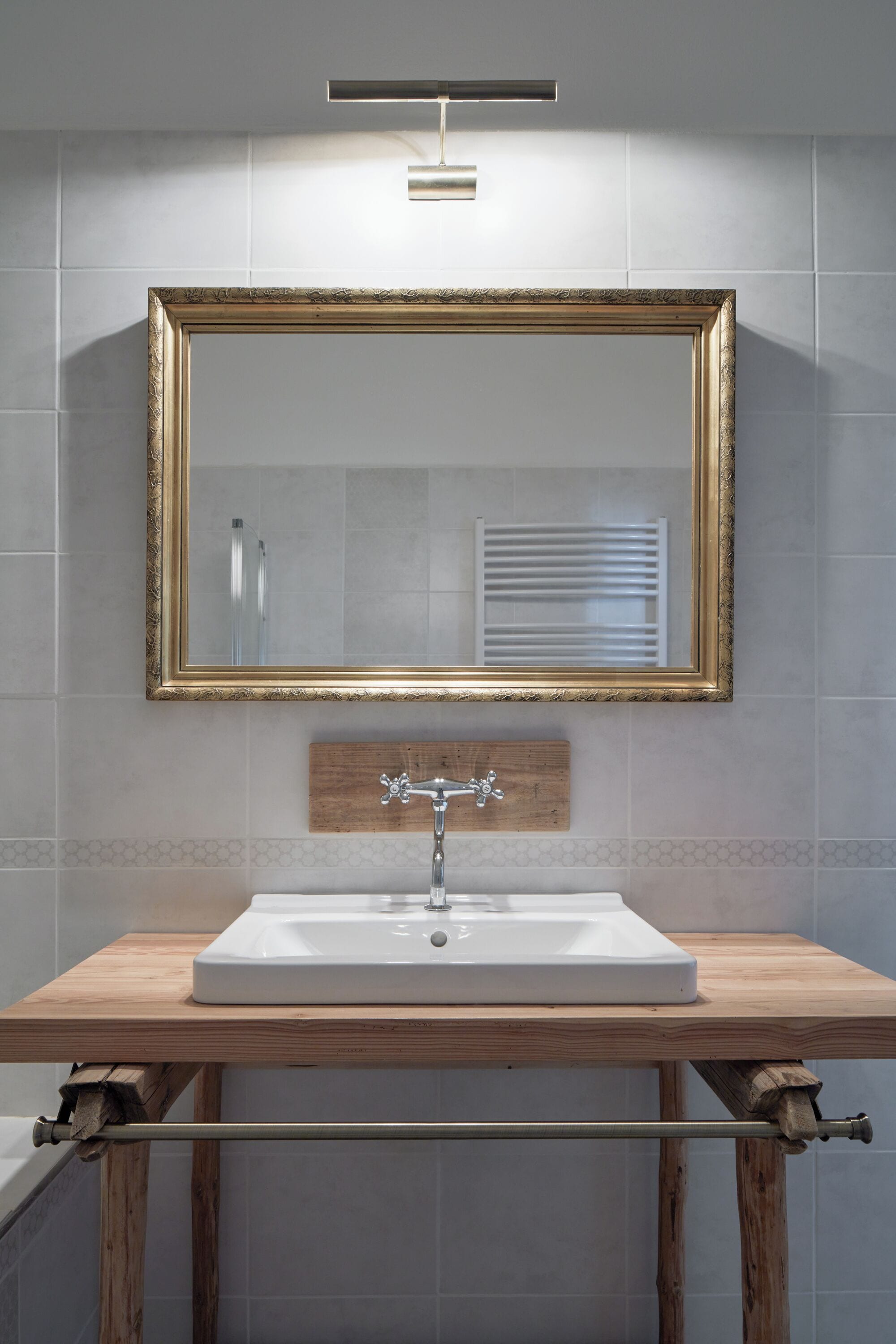 Une salle de bain avec un meuble-lavabo en bois, un lavabo blanc, un miroir avec un cadre doré et un porte-serviettes.
