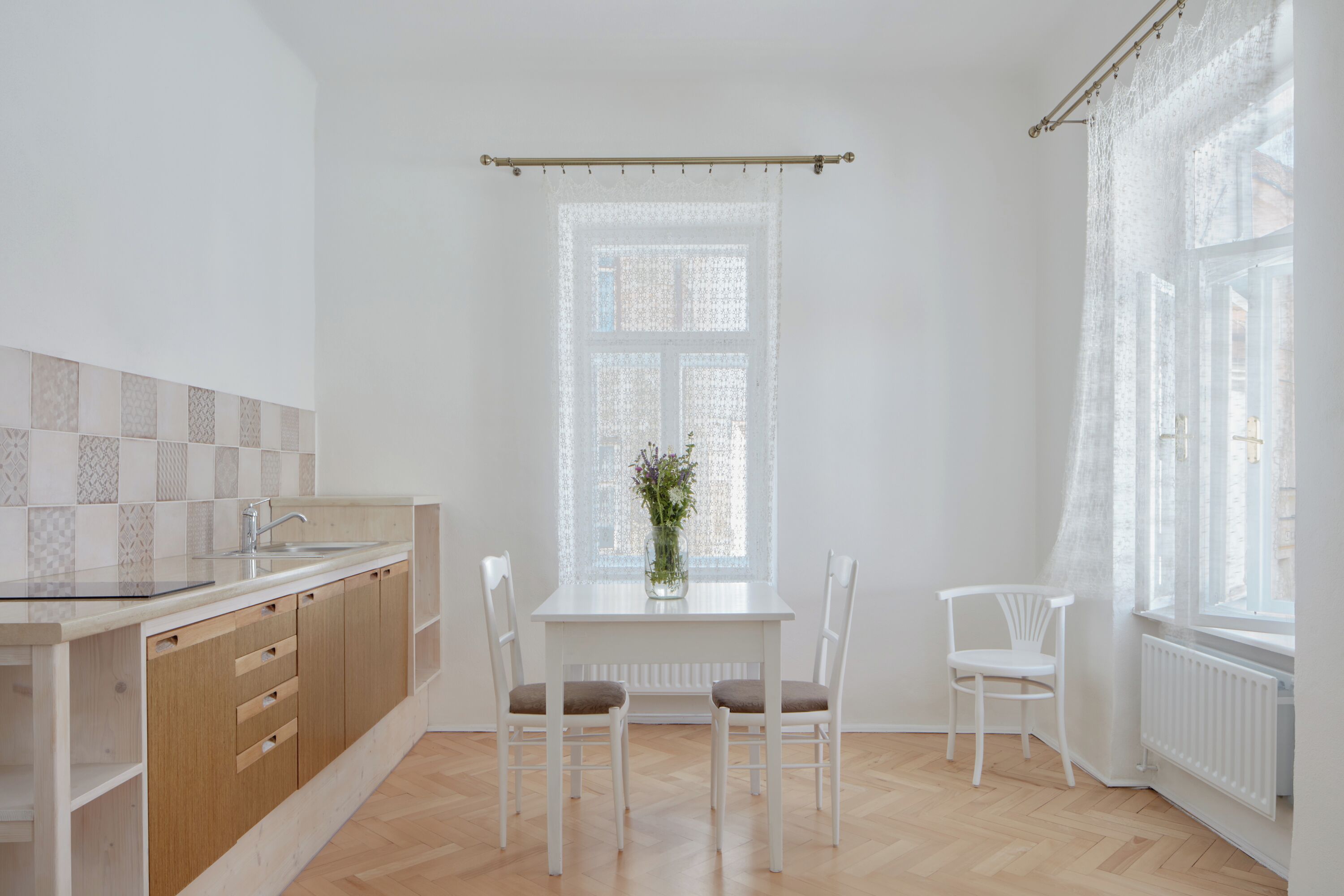 Et køkken med spisebord, stole, et vindue med gardin og en radiator.