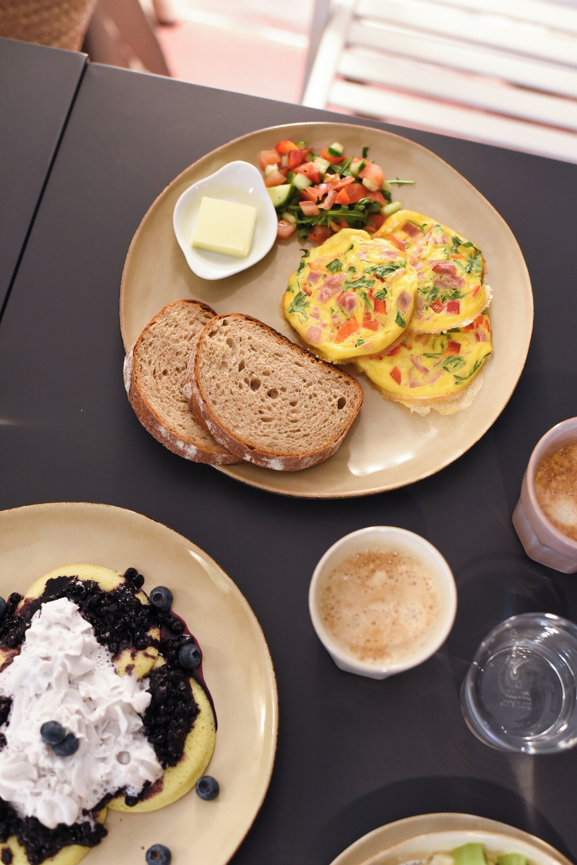 Une table avec une assiette de nourriture, un bol de beurre et une tasse de café.