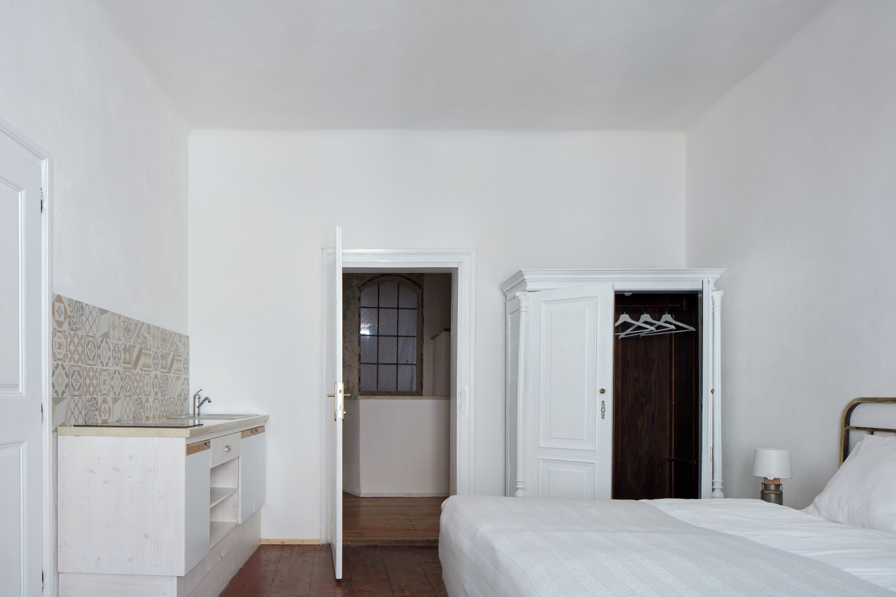 A bedroom with a bed, a wardrobe, a bathroom with a window, and a kitchenette with a sink and countertop.