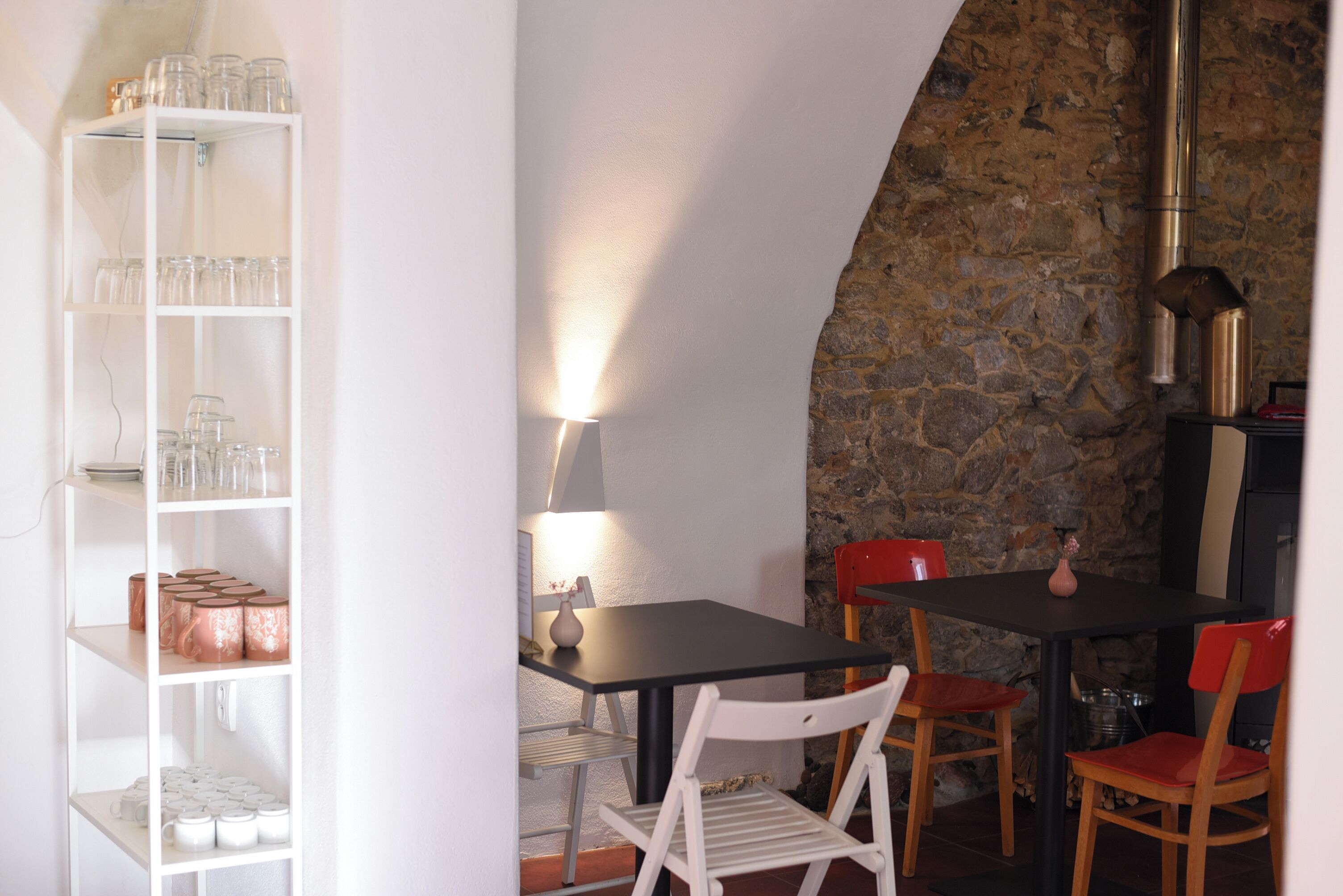 Un comedor con pared de piedra, una mesa negra y sillas blancas.