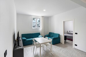 A compact living space with a white table, teal sofas, a TV on a stand, and a window with a view of the outside. - Apartment 'Via Leucosia' with Sea View, Wi-Fi and Air Conditioning (Salerno)