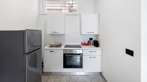 Eine kleine Küche mit Kühlschrank, Backofen, Spüle und weißen Schränken.