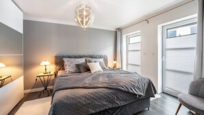 Ett sovrum med en säng, sänglampor, en globformad lampa och utsikt över omgivningen genom ett fönster.