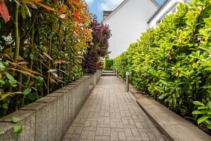Un sendero pavimentado bordeado de exuberante vegetación y un edificio blanco.