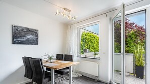 En matplats med ett bord, stolar och utsikt genom en glasdörr ut mot en trädgård.