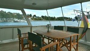 A boat deck with a wooden table and chairs, a clear view of the water and buildings in the background.