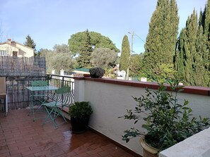 Un patio con una mesa, sillas, una planta en maceta y una pared con barandilla.