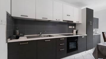 Een moderne keuken met donkere kastjes, witte aanrechtbladen en een ingebouwde oven.