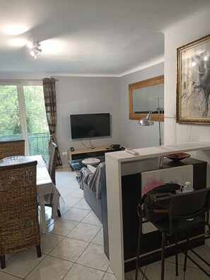 Ein modernes Zimmer mit Fernseher, Schreibtisch, Stuhl und einem großen Fenster mit Vorhängen.