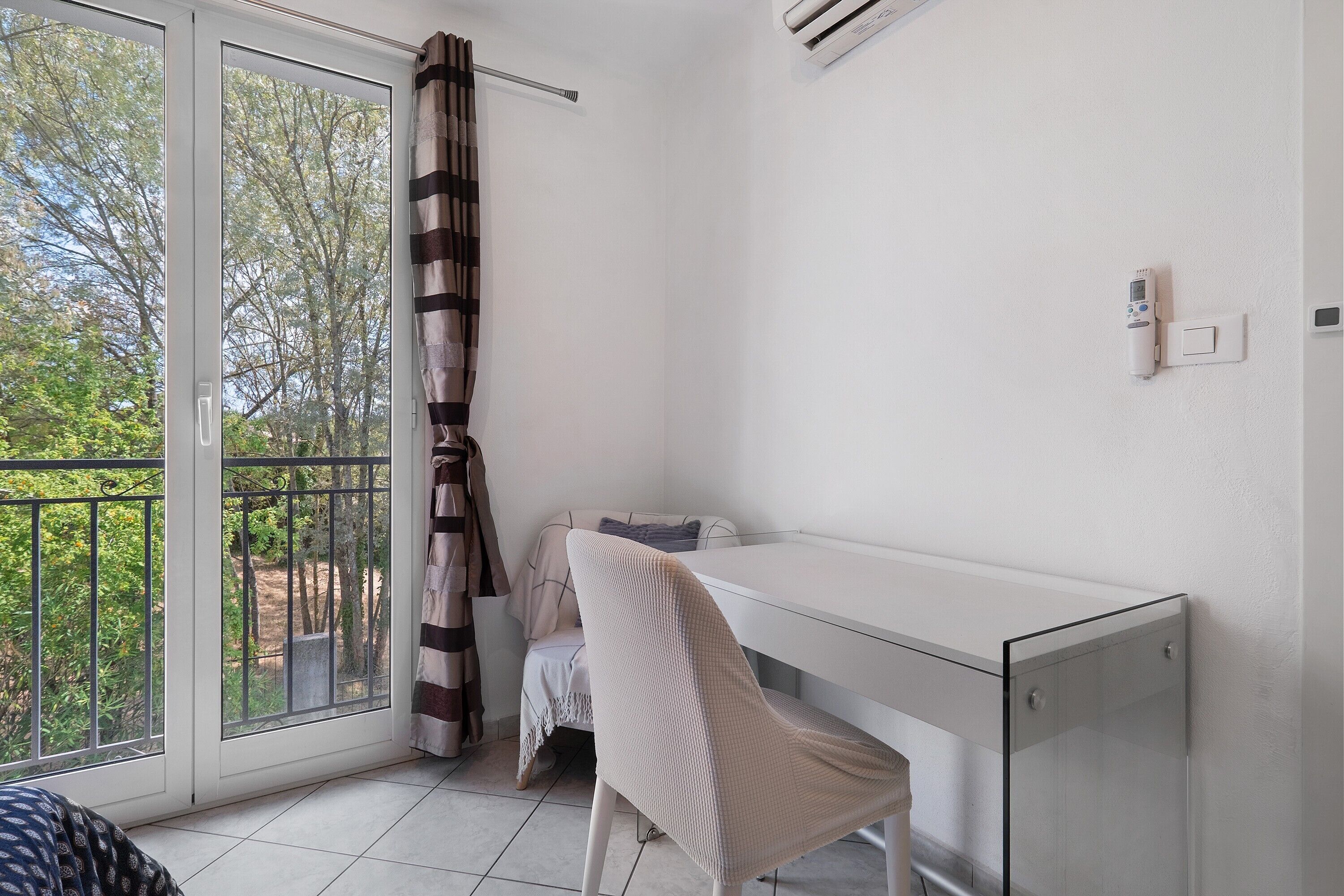 A room with a sliding glass door, a white desk, a chair, and a small table with a blanket.