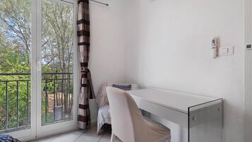 A room with a sliding glass door, a white desk, a chair, and a small table with a blanket.