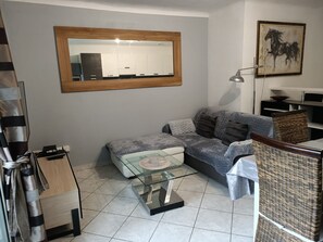 Ein Wohnzimmer mit Sofa, Hocker, Couchtisch aus Glas und einem Spiegel an der Wand.