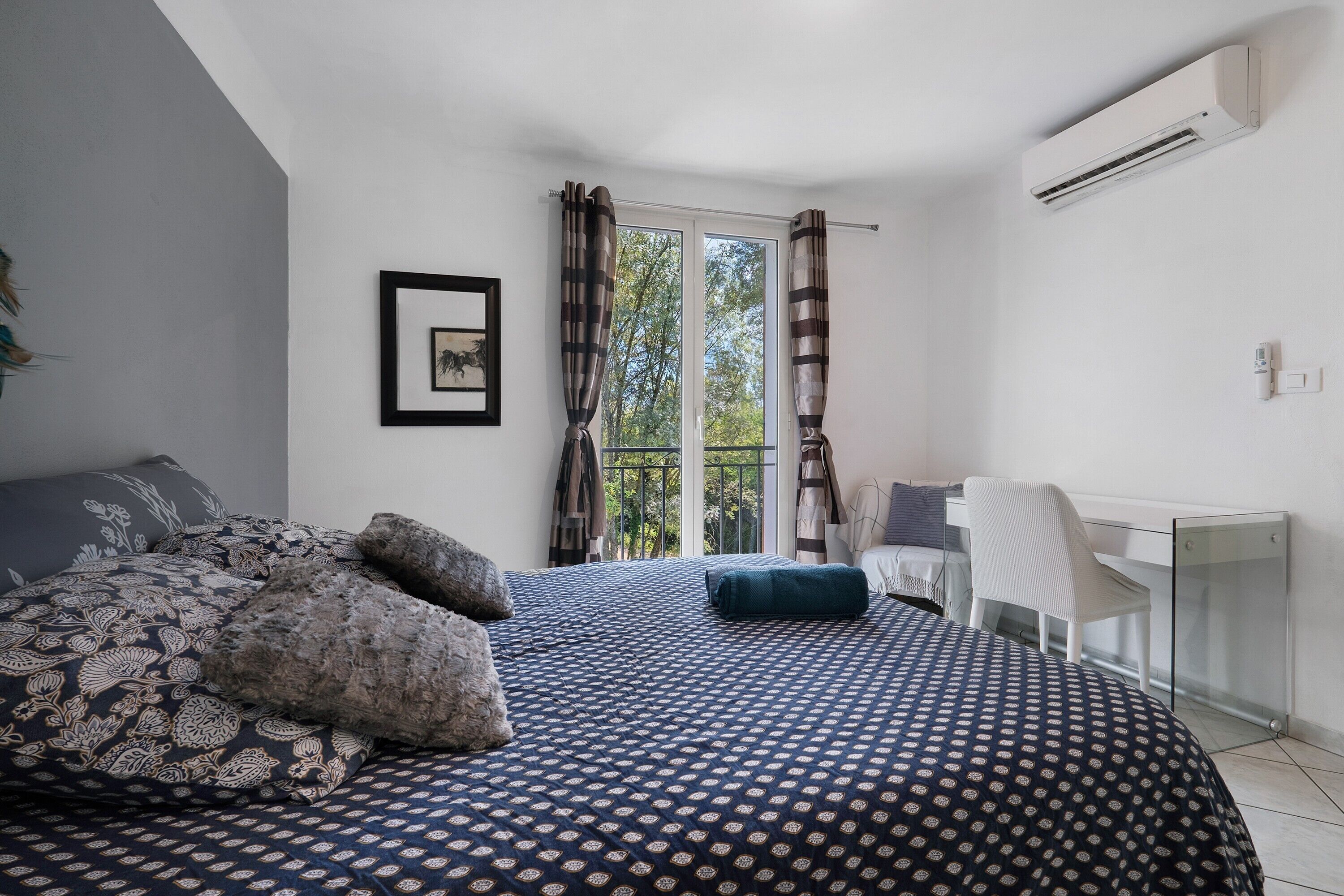 A bedroom with a bed, a desk, and an air conditioning unit.