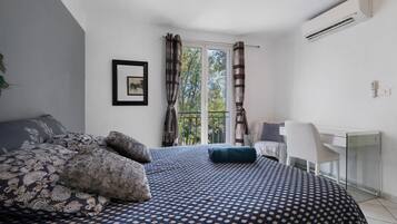 A bedroom with a bed, a desk, and an air conditioning unit.