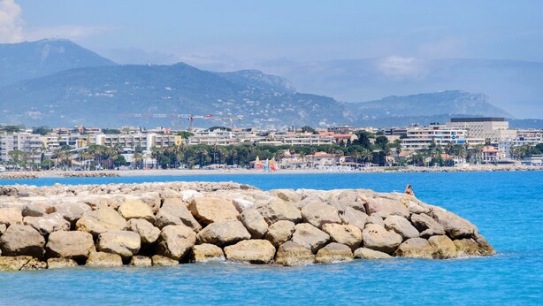 A coastal cityscape with a rocky breakwater, buildings, and mountains in the background. - Studio "Le Kennedy Bord De Mer" with Balcony, Wi-Fi and Air Conditioning (Cagnes-sur-Mer)