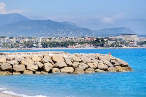 A coastal cityscape with a rocky breakwater, buildings, and mountains in the background. - Studio "Le Kennedy Bord De Mer" with Balcony, Wi-Fi and Air Conditioning (Cagnes-sur-Mer)