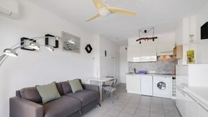 A modern apartment with a grey sofa, dining table, white kitchen, and a ceiling fan. - Studio "Le Kennedy Bord De Mer" with Balcony, Wi-Fi and Air Conditioning (Cagnes-sur-Mer)