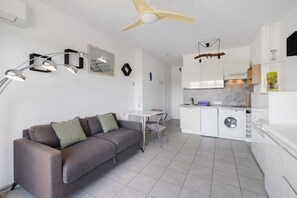 Een modern appartement met een grijze bank, eettafel, witte keuken en een plafondventilator.