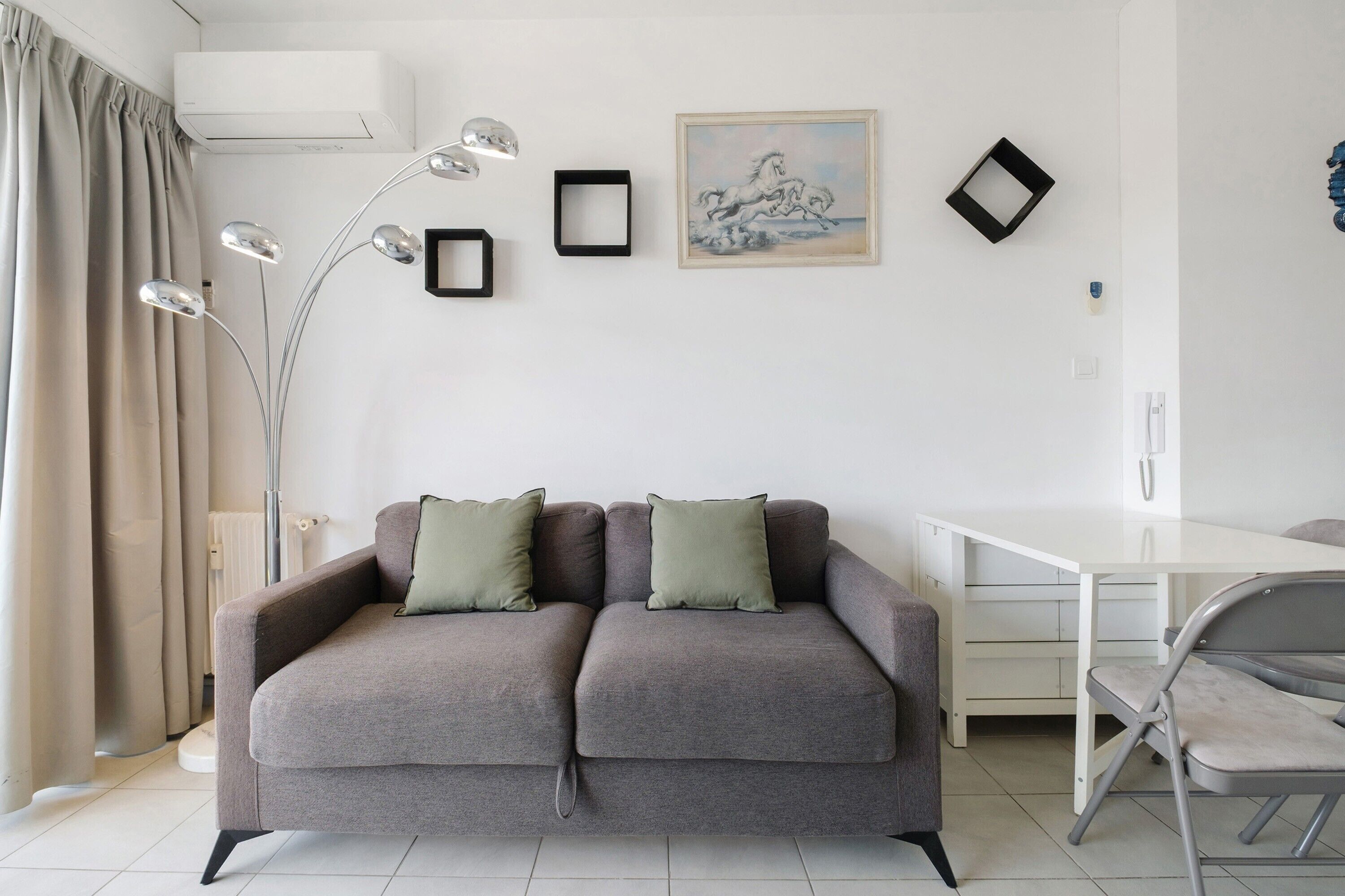 Un salon moderne avec un canapé gris, un bureau blanc et un grand lampadaire.