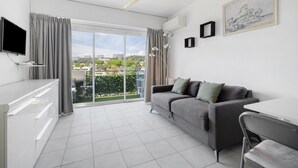 A modern living room with a sofa, a dining table, a TV, and a balcony with a view. - Studio "Le Kennedy Bord De Mer" with Balcony, Wi-Fi and Air Conditioning (Cagnes-sur-Mer)