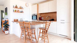 Una cocina moderna con una isla central, sillas de madera, armarios blancos y una lámpara colgante roja.