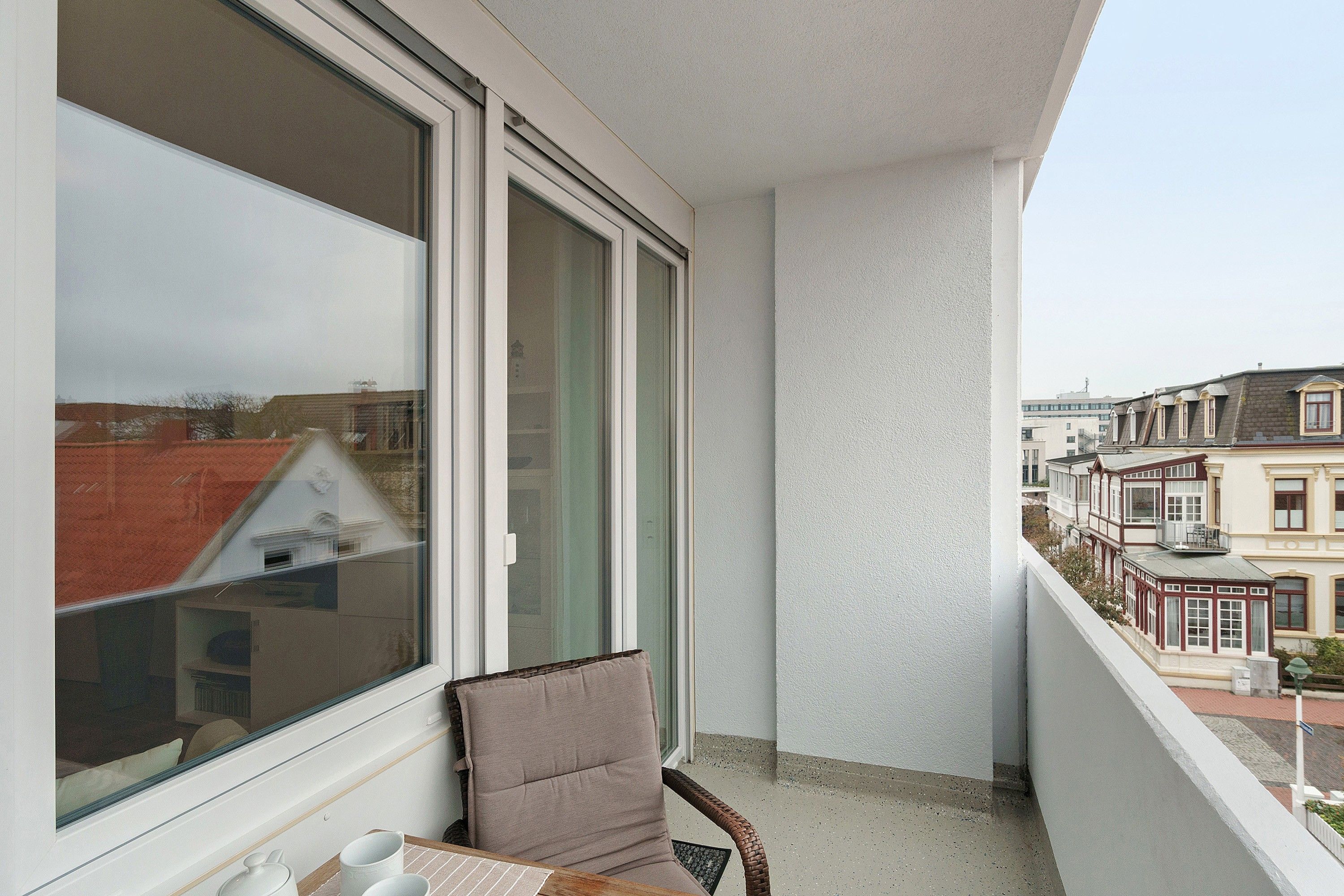 Ein Balkon mit Korbstuhl und Tisch, mit Blick auf eine Reihe traditioneller Häuser.