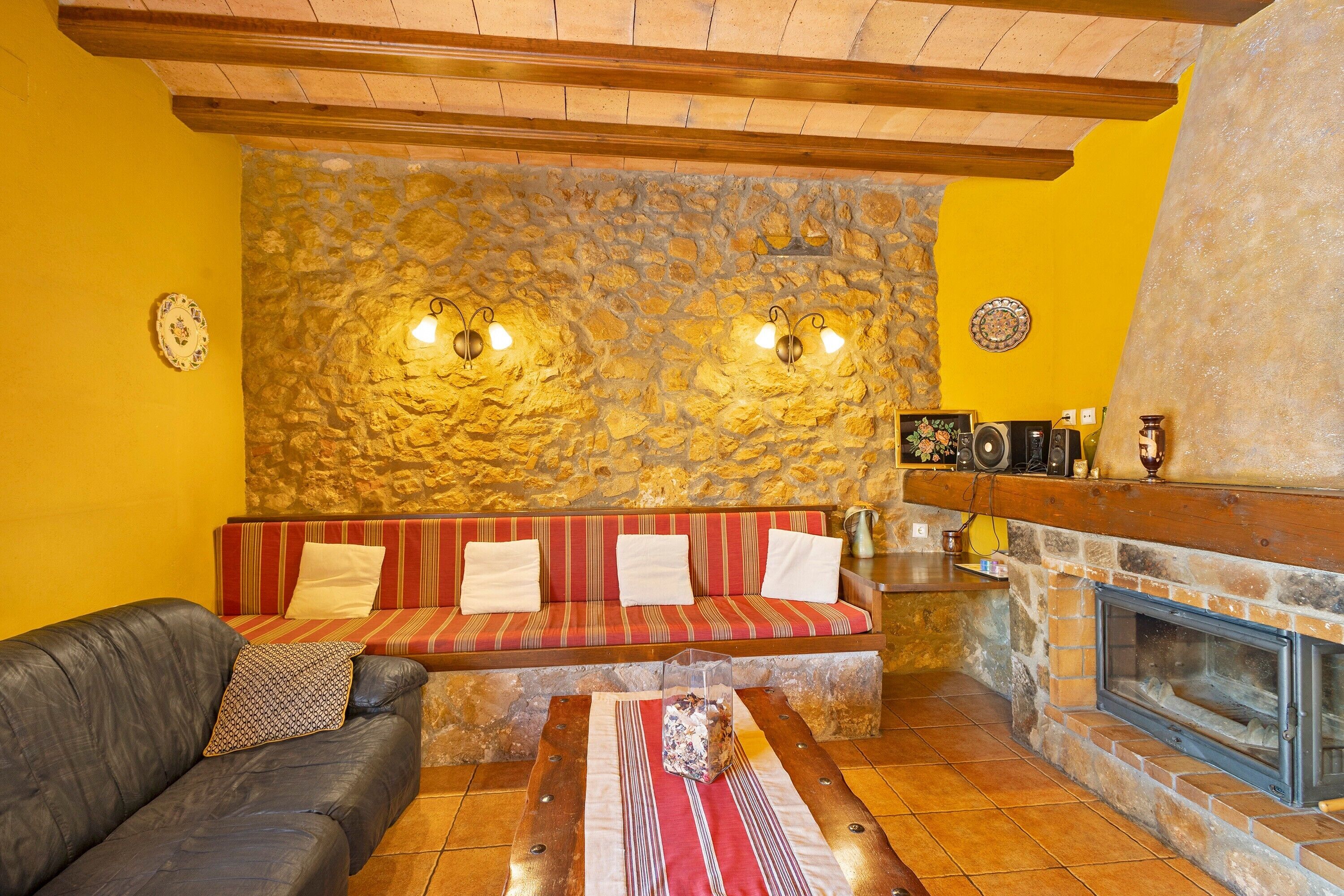 A cozy living room with a stone wall, a fireplace, a sofa, and a leather couch.