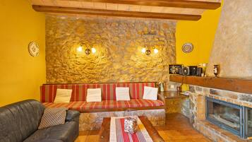A cozy living room with a stone wall, a fireplace, a sofa, and a leather couch.