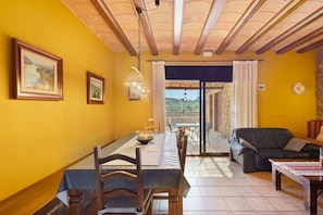 A dining area with a table set for two, a sofa, and a view through a glass door.