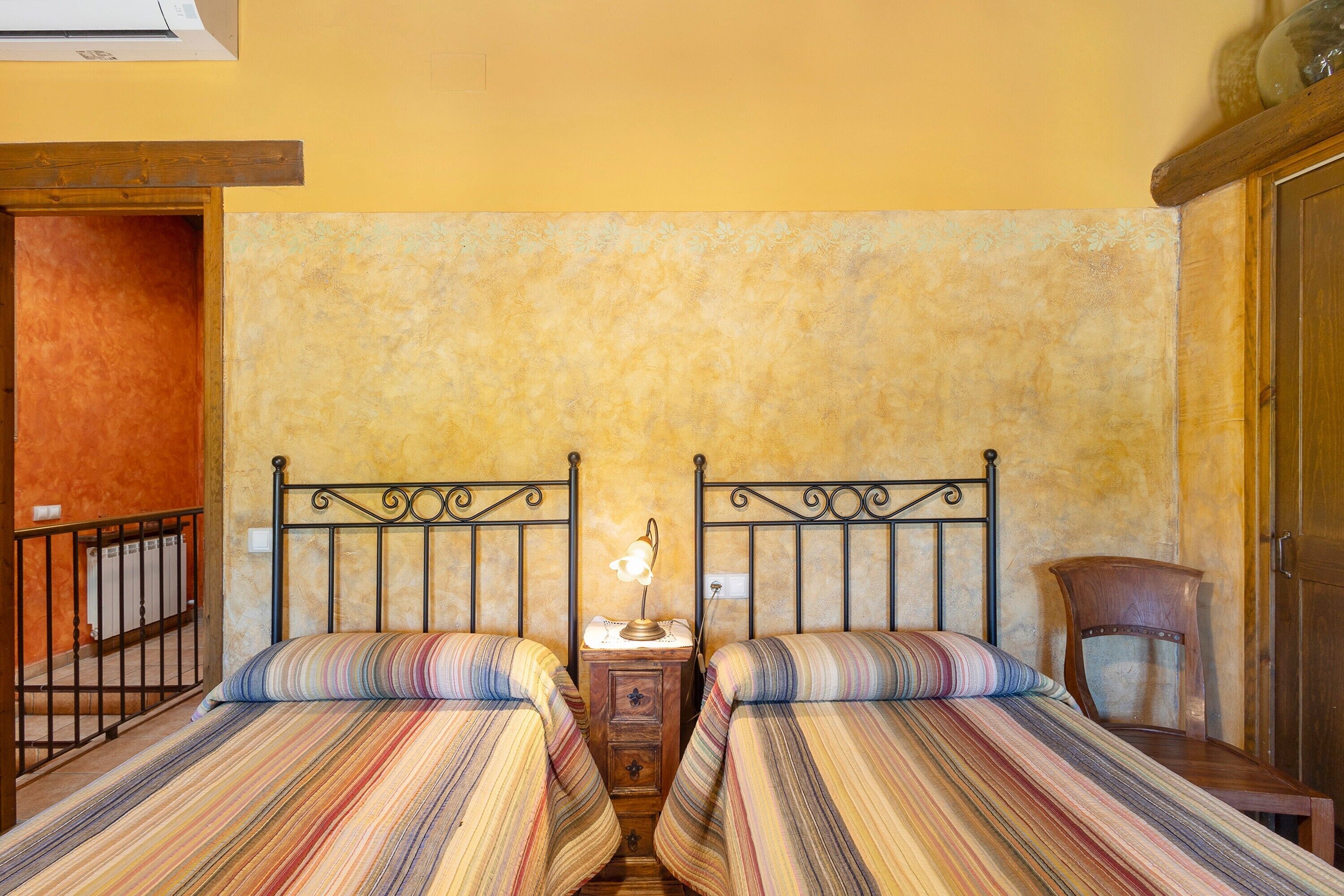 Una habitación con dos camas, una mesita de noche con lámpara, una silla de madera y un radiador.