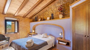 Une chambre à coucher comprenant un lit, une chaise, une table de chevet, une armoire en bois, un mur en pierre et une fenêtre.