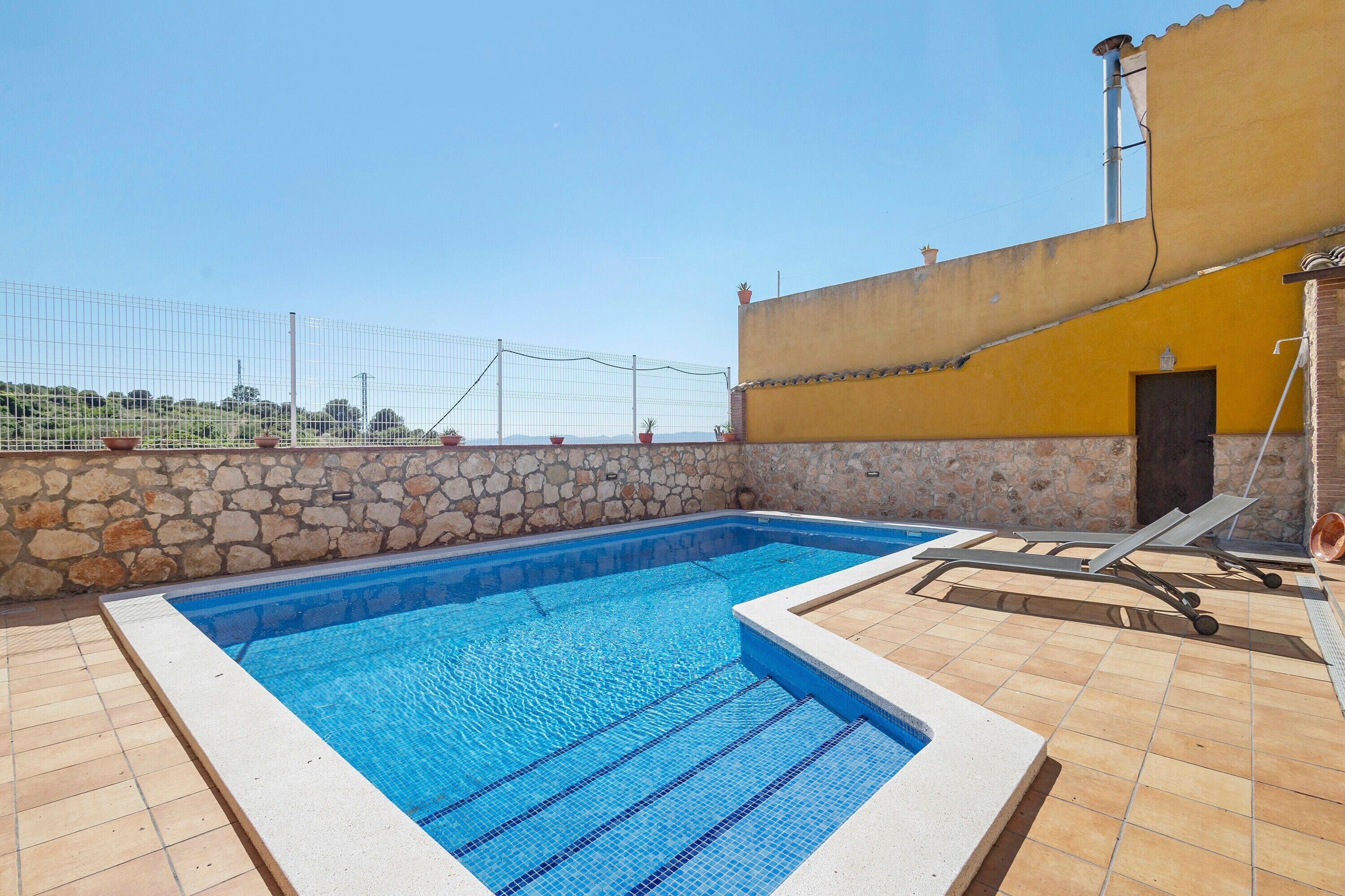 A swimming pool with a stone wall, a yellow building, and a clear sky.