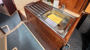 Une petite cuisine équipée avec un évier en acier inoxydable, des placards en bois et un petit plan de travail.