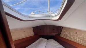 Une petite cabine dotée d’une lucarne, d’un lit avec des serviettes soigneusement pliées et d’une porte en bois.