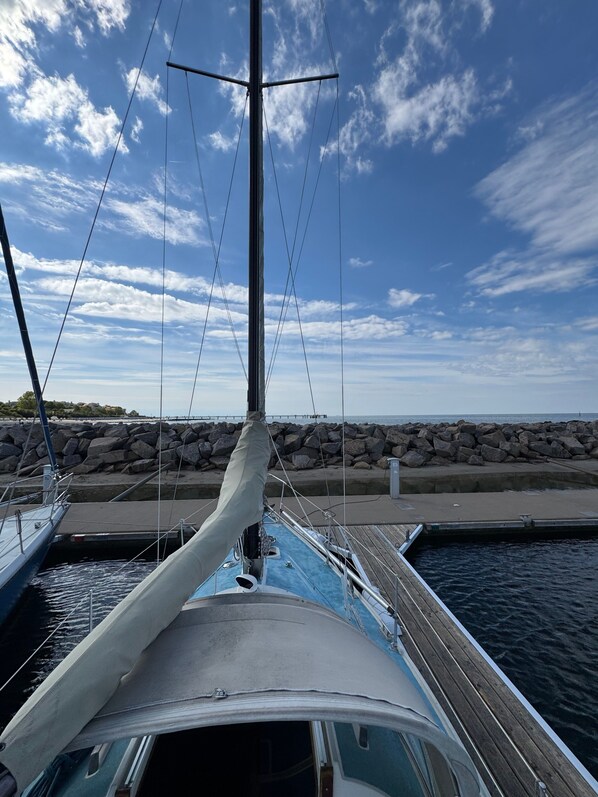 A sailboat docked at a marina with a rocky shoreline and a clear sky.