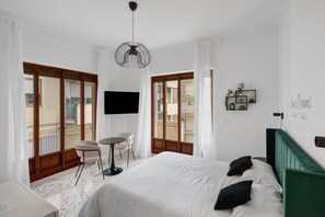 Ein Hotelzimmer mit Bett, Schreibtisch, Sessel, Fernseher und einem Balkon mit Vorhängen.