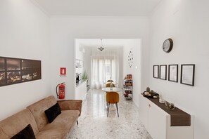 Ein modernes Wohnzimmer mit Sofa, einem Esstisch mit Stühlen, einer Küchenzeile und einem Flur, der zu einem weiteren Raum führt.