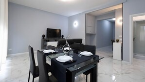 Zona pranzo moderna con tavolo in vetro, sedie nere e televisore a schermo piatto sullo sfondo.