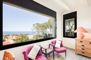 A room with a large window, a pink chair, a wooden chair, a small table, and a lamp. - Holiday Home 'Sa Punta 11' with Sea View, Private Pool and Wi-Fi (Sa Riera)