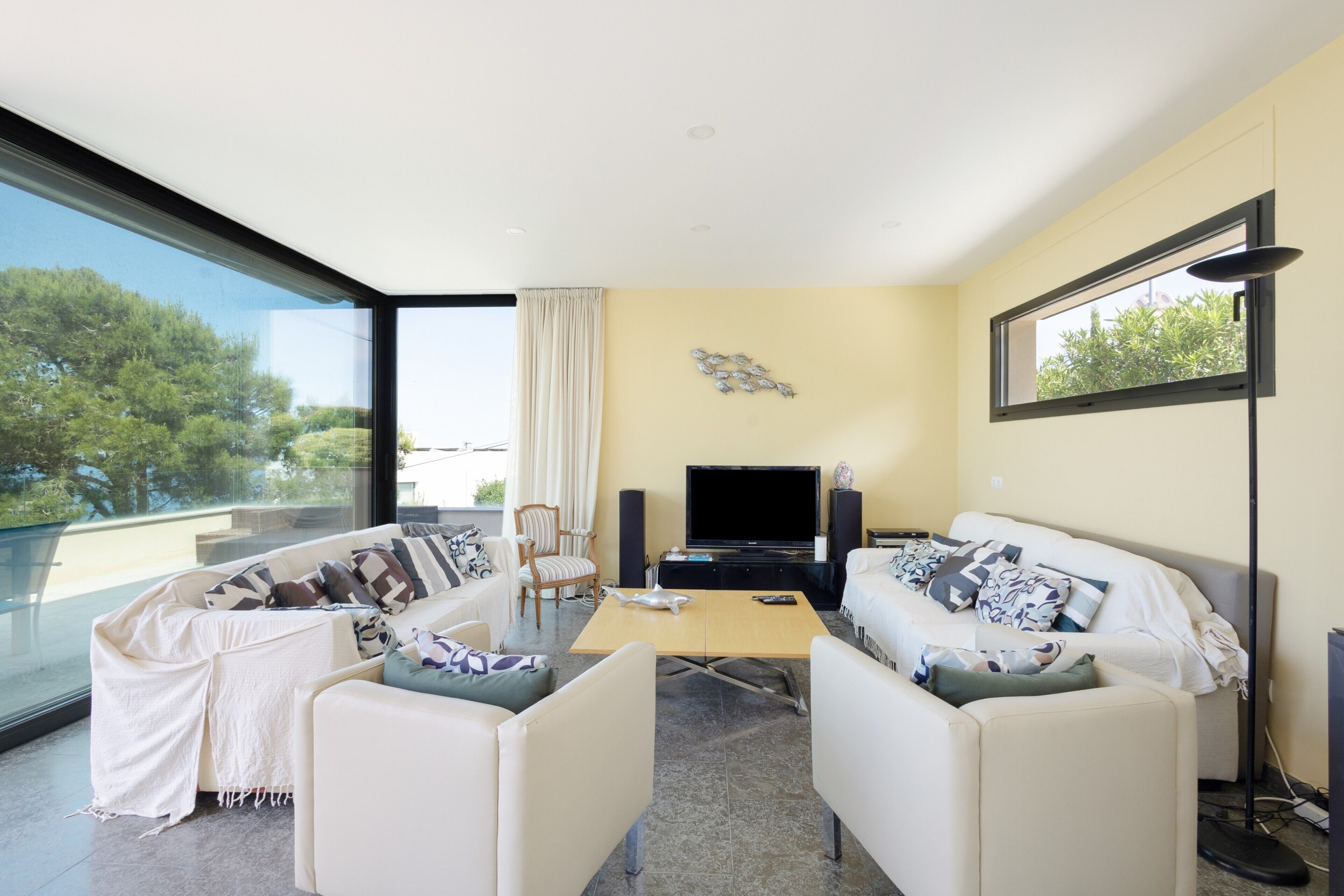 A modern living room with a large window, a flat-screen TV, and a sofa set.