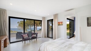 Ein Schlafzimmer mit einem großen Bett, zwei Sesseln, einem Schreibtisch und Meerblick.