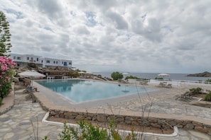 Zona de piscina con vistas al mar, camino de piedra y un edificio blanco.