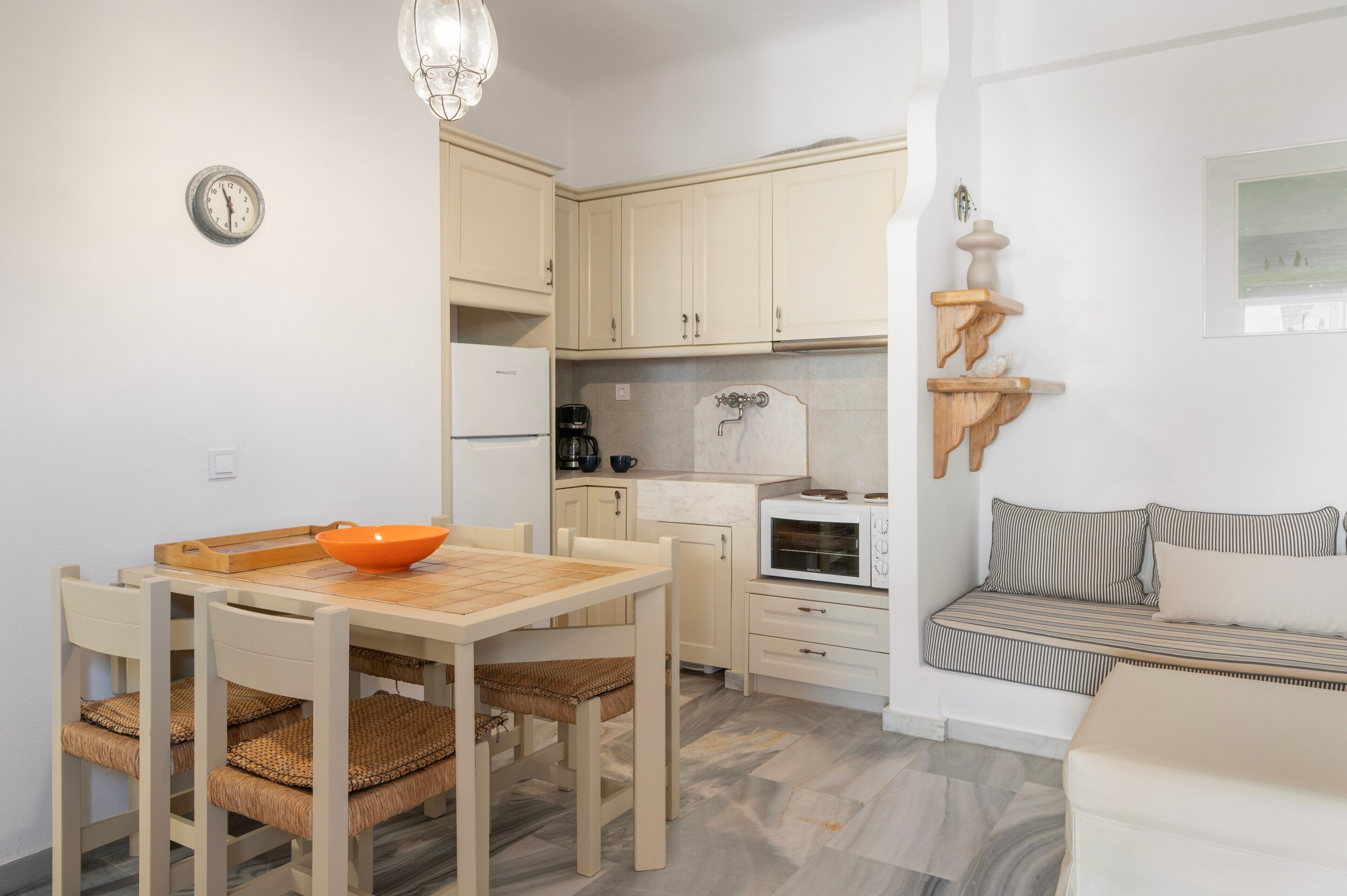 Une cuisine compacte avec des meubles blancs, une table à manger avec des chaises, une machine à café et un four à micro-ondes.
