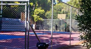 A fenced tennis court with a net, a basketball hoop, and a building in the background. - Dimelli's home in athens (Athens)