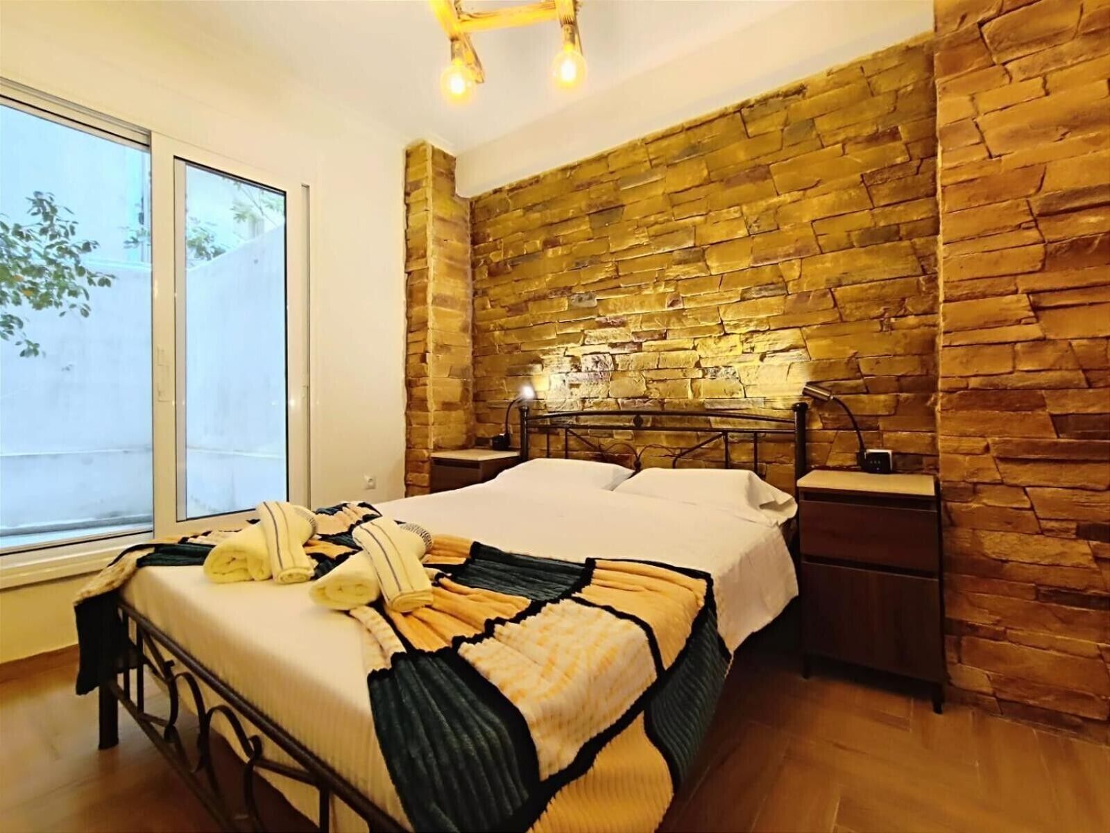 Une chambre avec un grand lit, une table de chevet, une lampe et un mur en briques.