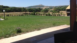 A patio with a view of a green field and distant hills. - Holiday Home 'Farm Holiday Sa Raighina - Right' with Shared Pool, Wi-Fi and Air Conditioning (Nulvi)