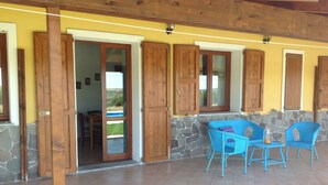 A covered patio area with stone walls, wooden doors, and blue wicker chairs. - Holiday Home 'Farm Holiday Sa Raighina - Right' with Shared Pool, Wi-Fi and Air Conditioning (Nulvi)