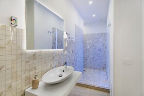 A modern bathroom with a large mirror, a sink, and a shower area. - Le Stanze In Centro – Quadruple Room (Naples)