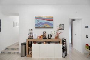 Ein moderner Wohnraum mit einem Holzkonsolentisch, einer Kaffeemaschine, einem Mülleimer und einem Bücherregal.
